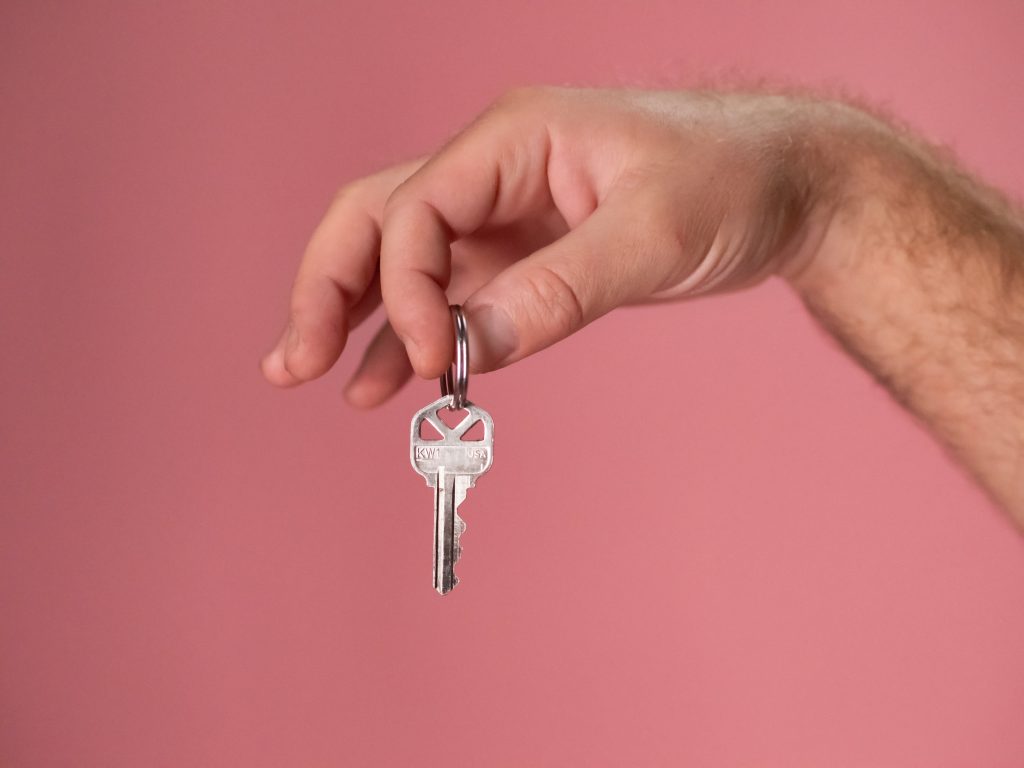 Hand met pols tegen roze achtergrond met tussen duim en wijsvinger een zilveren sleutel
