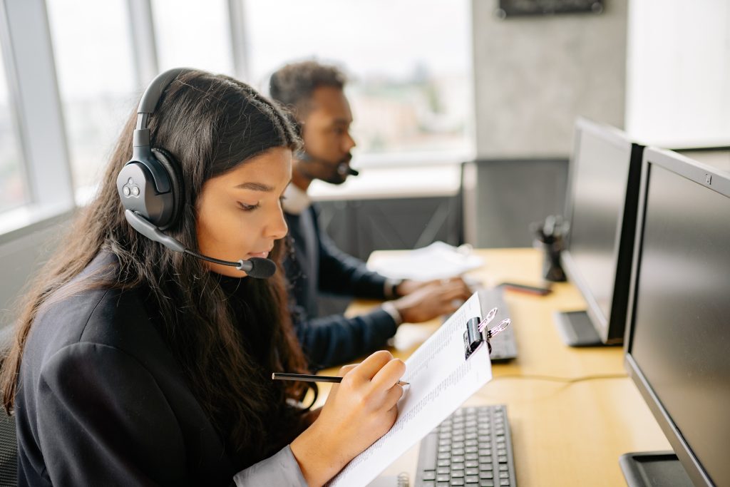 Vrouw en man achter laptop, zijaanzicht met koptelefoon en microfoon.