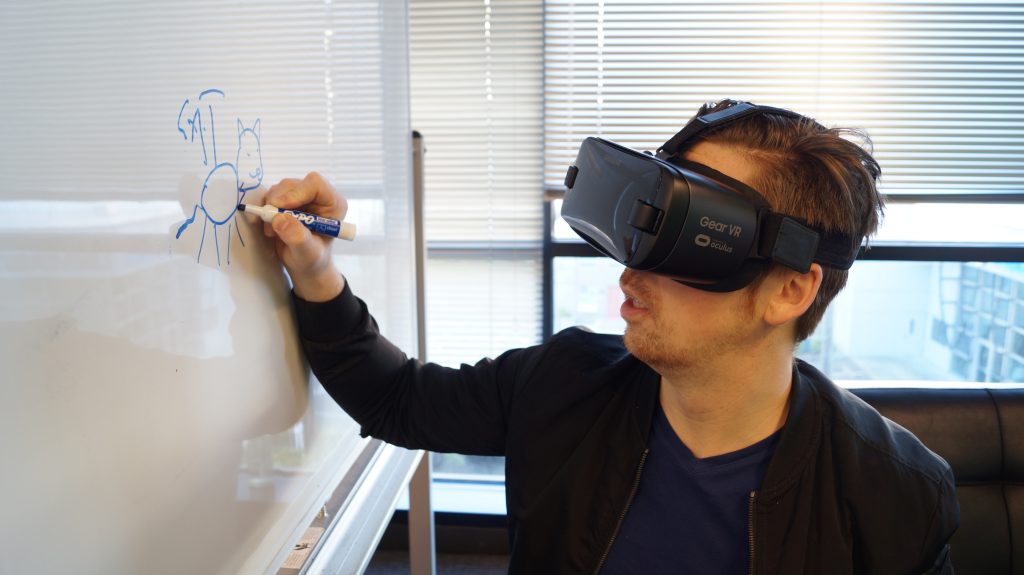 Docent met VR bril tekent met blauwe stift op whiteboard