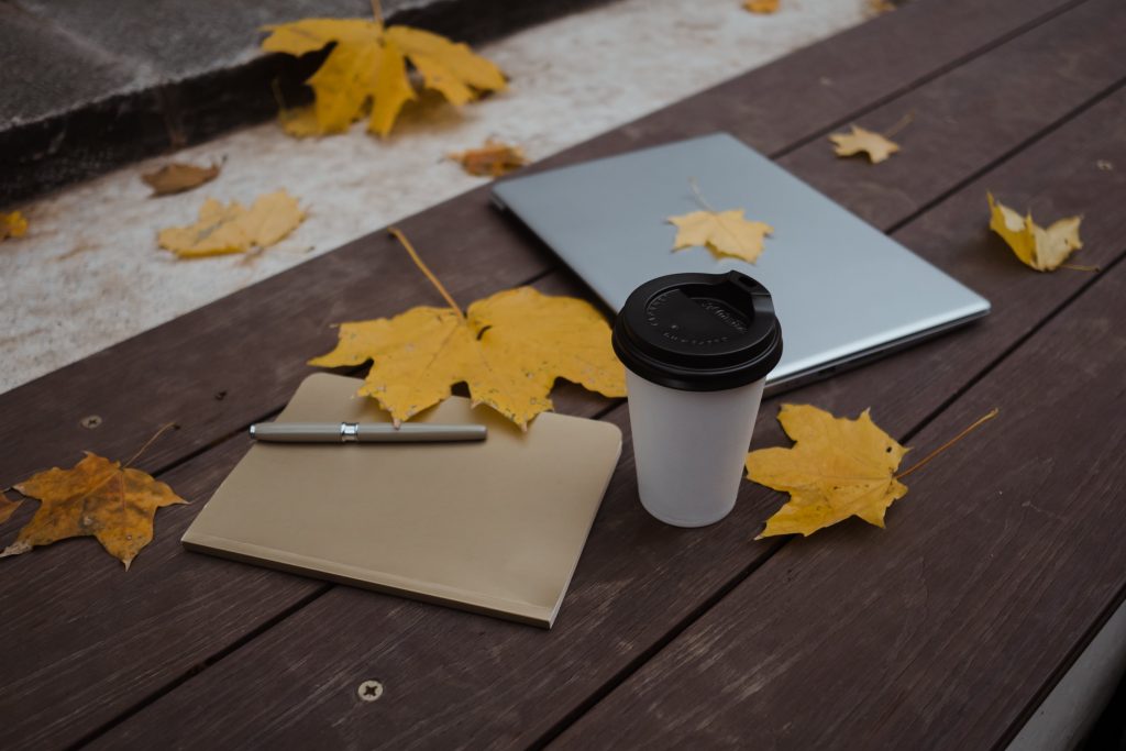 Laptop, ipad en koffiebeker op houten tafel met herfstbladeren.