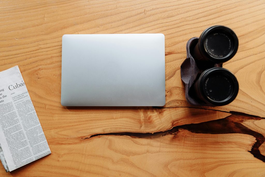 krant, laptop en verrekijker van bovenaf op een houten tafel