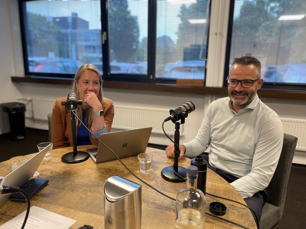 Foto aan tafel met rechts Marit Montsanto en links Martijn Timmer lachend achter de podcast microfoon