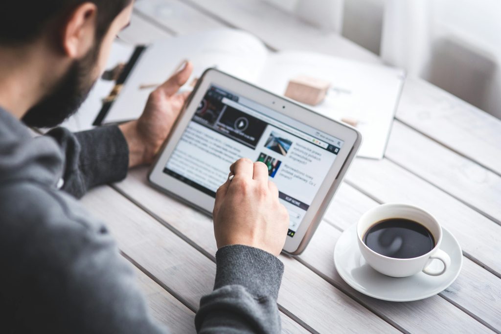 Man checkt nieuws op iPad met kop koffie aan tafel