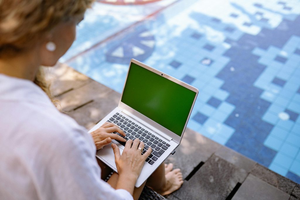 vrouw op achterzijde tikt op laptop aan zwembad