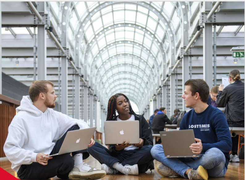 Stockfoto van drie studenten die op de grond zitten met een laptop op de schoot.