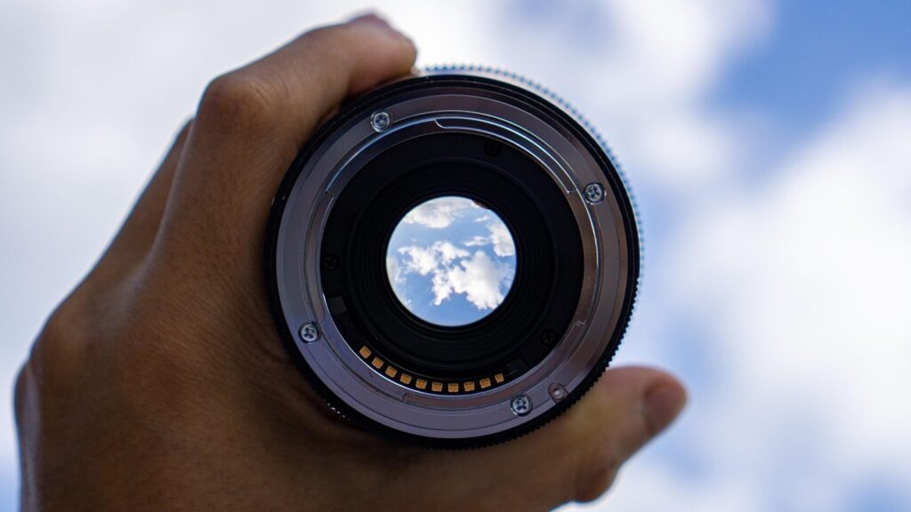 Hand met daarin een lens, met focus op wolk aan de hemel