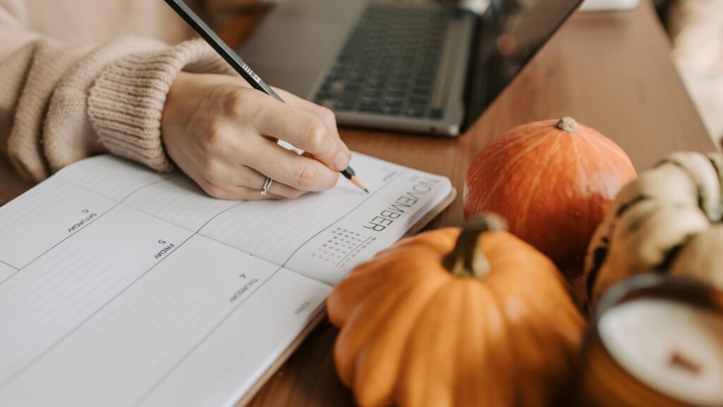 stilleven van pompoenen, met op achtergrond een hand met pen, agenda en laptop