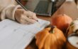 stilleven van pompoenen, met op achtergrond een hand met pen, agenda en laptop